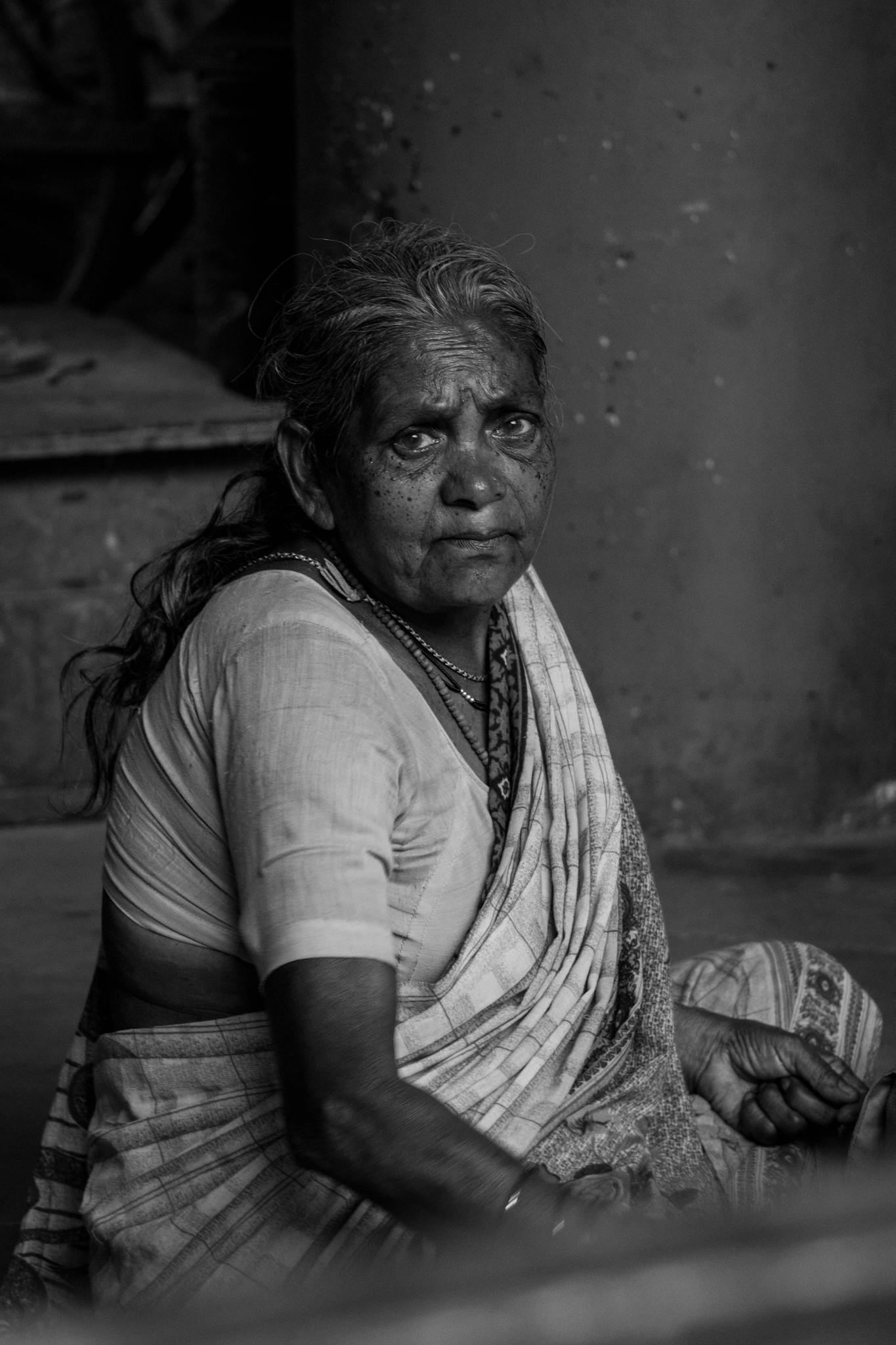 Black and white portrait of an elderly Indian woman sitting indoors in traditional attire.